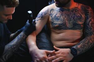 masculino tatuaje artista participación un tatuaje pistola, demostración un proceso de haciendo tatuajes en un masculino tatuado del modelo brazo foto