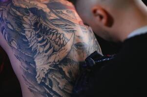 Shot of a tattoo artist hands forming perfect lines on man back with ink photo