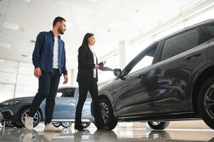 sonriente coche vendedor en pie en coche salón con cliente y demostración alrededor carros en rebaja foto