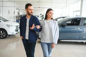 es el único coche que quiero. Hermosa joven pareja de pie en el concesionario eligiendo el coche para comprar foto