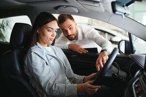 Satisfied happy caucasian female client customer woman sitting at the wheel of new car while male shop assistant helping her choose it photo