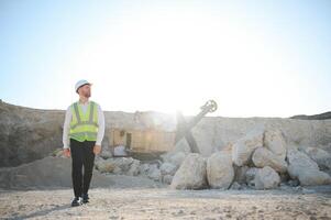 A worker in a helmet stands on the background of an excavator in a quarry photo