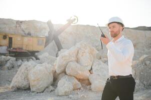 A worker in a helmet stands on the background of an excavator in a quarry photo