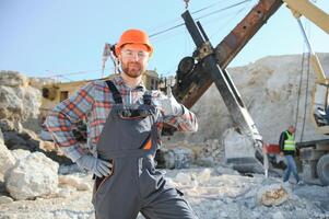 A worker in a helmet stands on the background of an excavator in a quarry photo