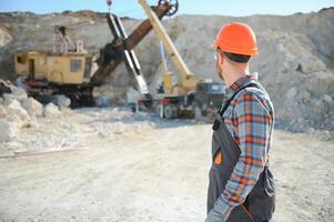 A worker in a helmet stands on the background of an excavator in a quarry photo