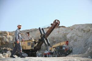 A worker in a helmet stands on the background of an excavator in a quarry photo