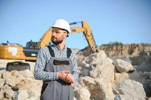 A worker in a helmet stands on the background of an excavator in a quarry photo