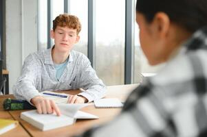 students sit at shared desk making notes studying together at university photo