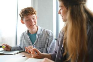 students sit at shared desk making notes studying together at university photo