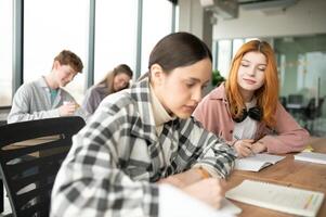 estudiantes sentar a compartido escritorio haciendo notas estudiando juntos a Universidad foto