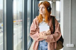 Red-haired student girl stands by the window with books and a backpack photo