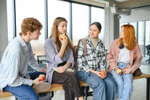 alegre estudiantes son sentado a escritorios y comiendo un manzana durante un descanso foto