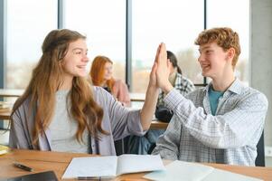 students sit at shared desk making notes studying together at university photo