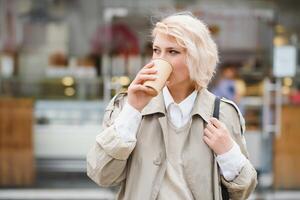 alegre elegante joven mujer en el calle Bebiendo Mañana café en Brillo Solar ligero. foto