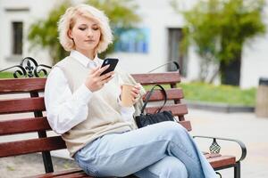 hermosa elegante mujer teniendo bueno Moda ropa caminando en calle y Bebiendo algunos café en taza para llevar con bueno verano estado animico cerca calle cafetería. foto