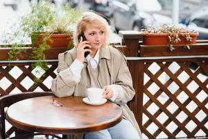 Very beautiful young woman, sit in Cafe and drink coffee or tea, street front view photo