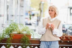 Very beautiful young woman, sit in Cafe and drink coffee or tea, street front view photo