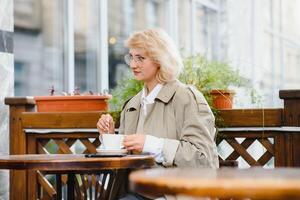 Very beautiful young woman, sit in Cafe and drink coffee or tea, street front view photo