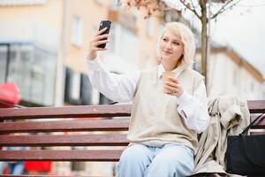 hermosa elegante mujer teniendo bueno Moda ropa caminando en calle y Bebiendo algunos café en taza para llevar con bueno verano estado animico cerca calle cafetería. foto