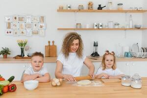 contento familia en el cocina. madre y niños preparando el masa, hornear galletas foto