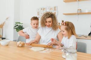 contento familia en el cocina. madre y niños preparando el masa, hornear galletas foto