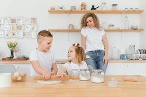 contento familia en el cocina. madre y niños preparando el masa, hornear galletas foto