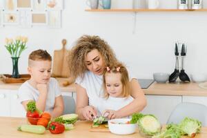 mother with children preparing vegetable salad at home photo