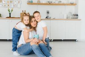 Happy young family, mom with little children sit on warm wooden floor in new modern design kitchen, mother with excited small kids relax rest in own renovated apartment, moving concept photo