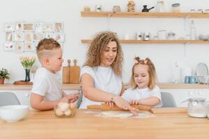 contento familia en el cocina. madre y niños preparando el masa, hornear galletas foto