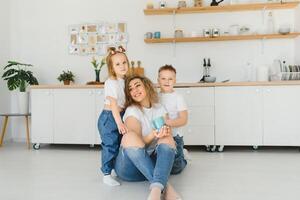 Happy young family, mom with little children sit on warm wooden floor in new modern design kitchen, mother with excited small kids relax rest in own renovated apartment, moving concept photo