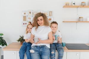 Mom with her two children sitting on the kitchen table. Mother with daughter and toddler son having breakfast at home. Happy lifestyle family moments. photo