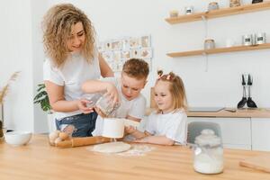 contento familia en el cocina. madre y niños preparando el masa, hornear galletas foto