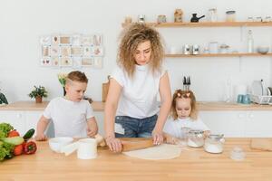 contento familia en el cocina. madre y niños preparando el masa, hornear galletas foto