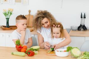 Young mother and her two kids making vegetable salad photo