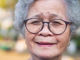 Close-up of face elderly woman smiling happiness, short gray hair and looking at the camera while standing outdoors. Concept of aged people and healthcare photo