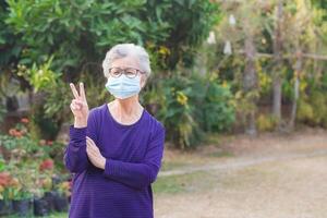 Portrait of a senior woman wearing a face mask and looking at the camera while standing in a garden. Space for text. Concept of aged people and healthcare photo