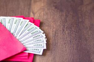 Close-up of a red envelope packet with money dollars on wooden table background. Space for text. Concept of money photo