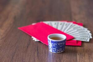 de cerca de un taza para té y rojo sobres paquete con nosotros billetes o ang pao preparar para dando a niños en chino nuevo año. de madera mesa antecedentes y espacio para texto. festival concepto foto