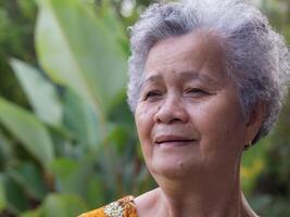 retrato de un mayor mujer con corto gris pelo sonriente y mirando lejos mientras en pie en el jardín. espacio para texto. concepto de Envejecido personas y cuidado de la salud foto