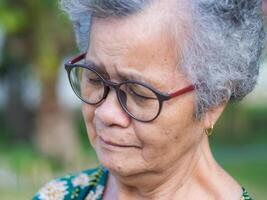 Close-up of face senior woman with short gray hair, wearing glasses and eyes close while standing in a garden. Concept of aged people and healthcare photo