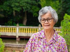 Senior woman wearing glasses smiling and looking at the camera while standing in the garden. Space for text. Concept of aged people and healthcare photo
