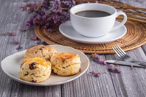 de cerca de tradicional británico bollos y un Galleta en un plato con un taza para té y flor borroso antecedentes. espacio para texto foto