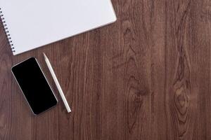 Top view of a sketchbook, smartphone, and pencil placed on wooden table. Template for text. Wood texture background. Concept of drawing and technology photo