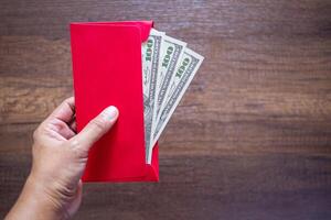 Close-up of hand holding a red envelope packet with money dollars or Ang Pao prepare for given to children during Chinese New Year for a blessing. Space for text. Festival concept photo