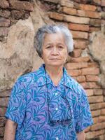 Asian Senior woman looking at camera while standing with brick background photo