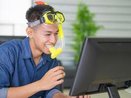 Young man wearing a diving mask yellow and sitting on a chair working in the office. He dreams of the sea because the holiday coming soon. Holiday concept photo