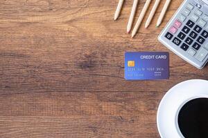 Top view of a blue credit card, pencil, calculator, coffee cup on a wooden table in the office. Space for text. Wood texture background. Business and finance concept photo