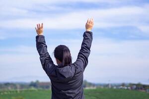 Back view of a woman standing and hands up at tea plantation. Space for text. Concept of people and travel photo