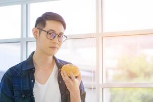 Young man holding bread and looking at the camera while standing in the living room at home. Fresh bakery product. Foods concept photo