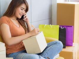 mujer de negocios utilizando un teléfono inteligente, sonriente y escribir datos en cubrir paquete o empaquetar caja para preparar enviar a cliente. concepto de negocio y comercio electrónico foto